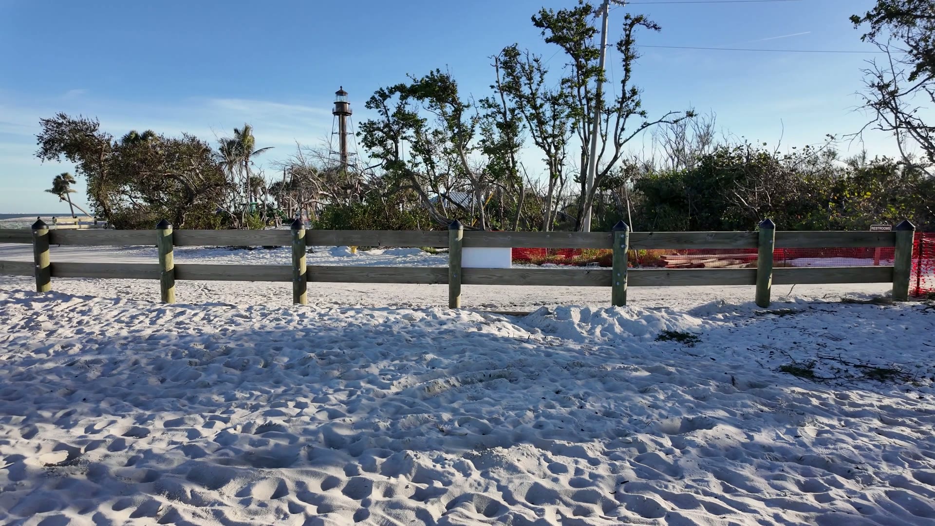 The Sanibel Island lighthouse rising above beach trees behind a wooden dune fence