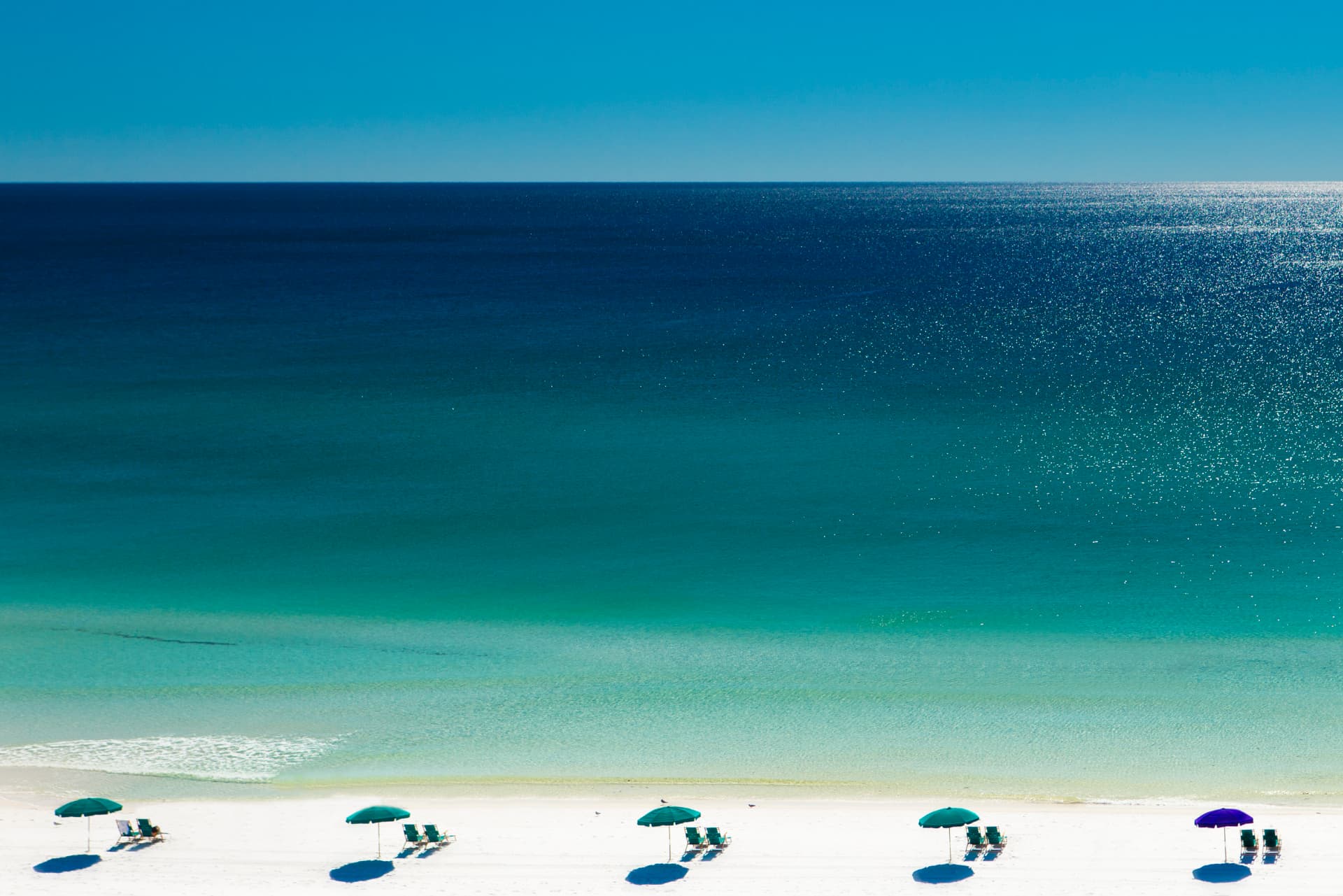 Beach umbrellas and deck chairs on white sand beside turquoise Gulf water in Destin, Florida